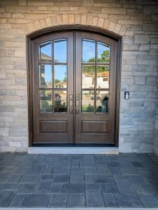 Double wooden front doors with grid glass panels set in a stone facade and arched transom above.